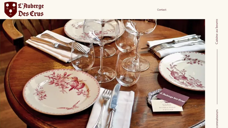 Page d'accueil de L'Auberge des Crus : blason bordeaux et grande photo d'une table dressée avec assiettes anciennes et verres à vin.